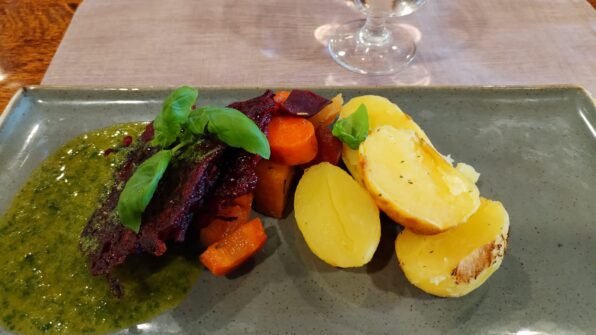 Planetaarinen ateria lautasaella: kasvispihvi, yrttiperunat, uunijuurekset, vegaaninen yrttikastike